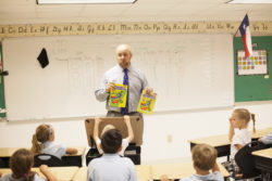 A teacher shows coloring books to a class, while one young lady gives a controlled salute