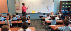 A teacher gestures to the class verbosely as she teaches